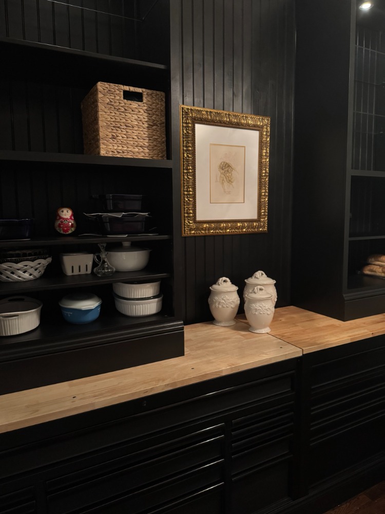 A walk-in pantry with black beadboard walls, open shelving and a butcher block counter, built in a former formal dining room.