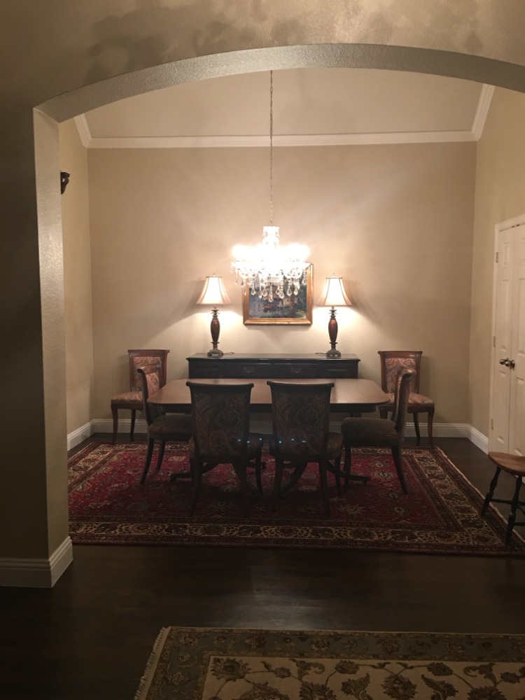 The original formal dining room seen from the entry hall through a wide arched opening. A six-chair table and a crystal chandelier fill most of the narrow room, leaving little space to walk behind the chairs.