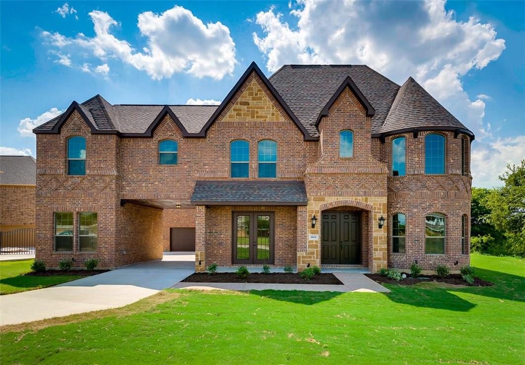 A large two-story brick and stone home with a corner turret and a wide manicured lawn, in the Grand Peninsula neighborhood of Grand Prairie.